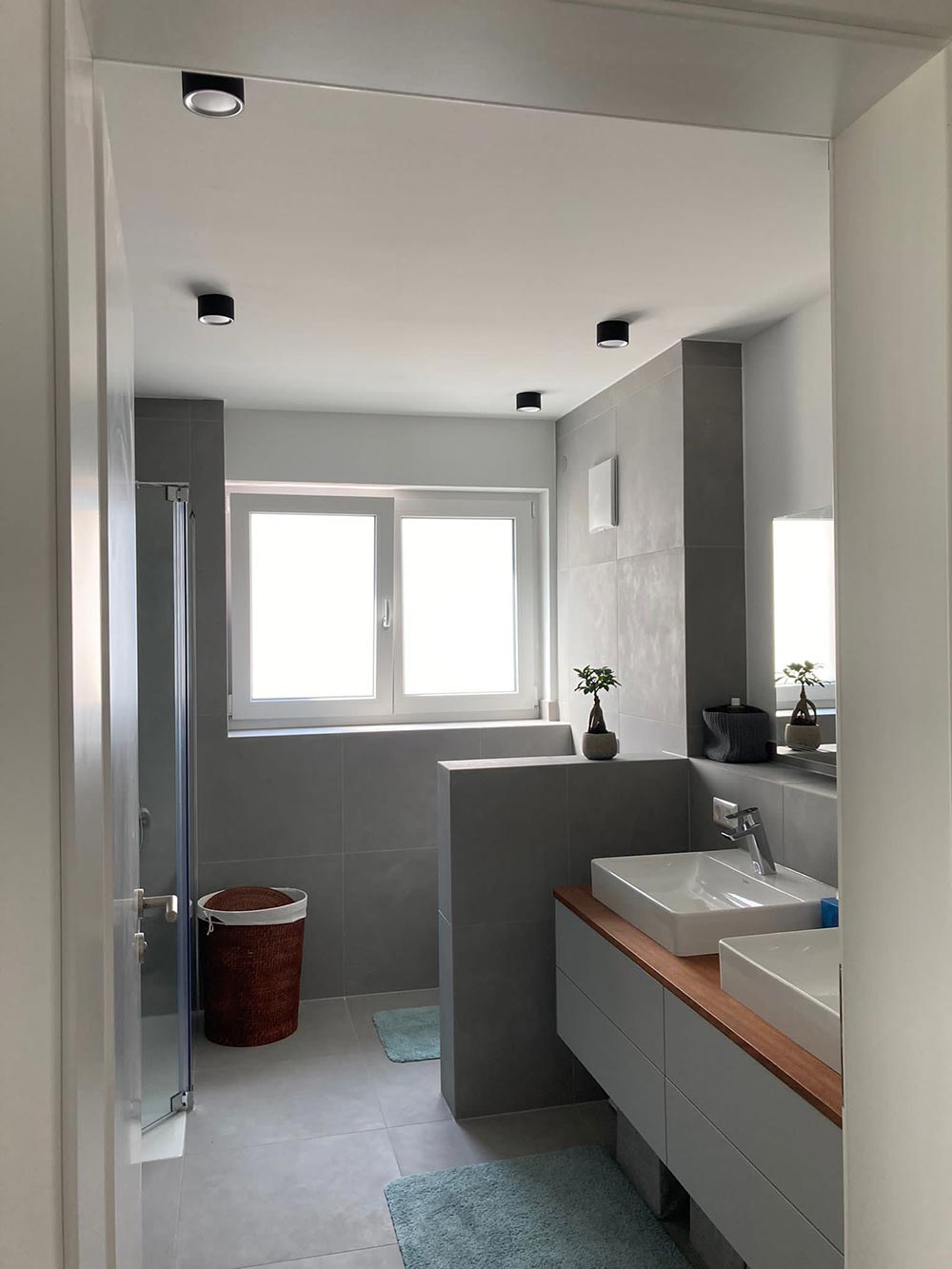 Modernes Bad in Grau und Weiß mit Fenster, Doppelwaschbecken und Pflanzen