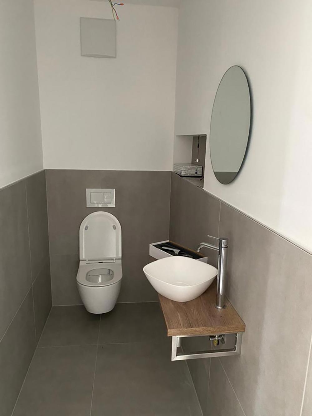 Modernes grauweisses Bad mit WC, Waschbecken, Holzablage und Rundspiegel
