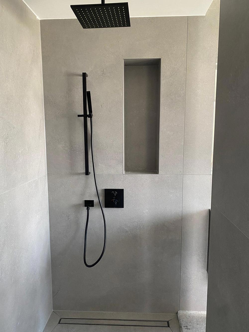 Moderne graue Dusche mit schwarzem Regenduschkopf und Wandnische